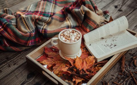 mug of coffee with marshmallow in front of open book on tray