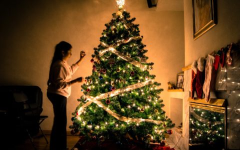 child standing in front of Christmas tree with string lights