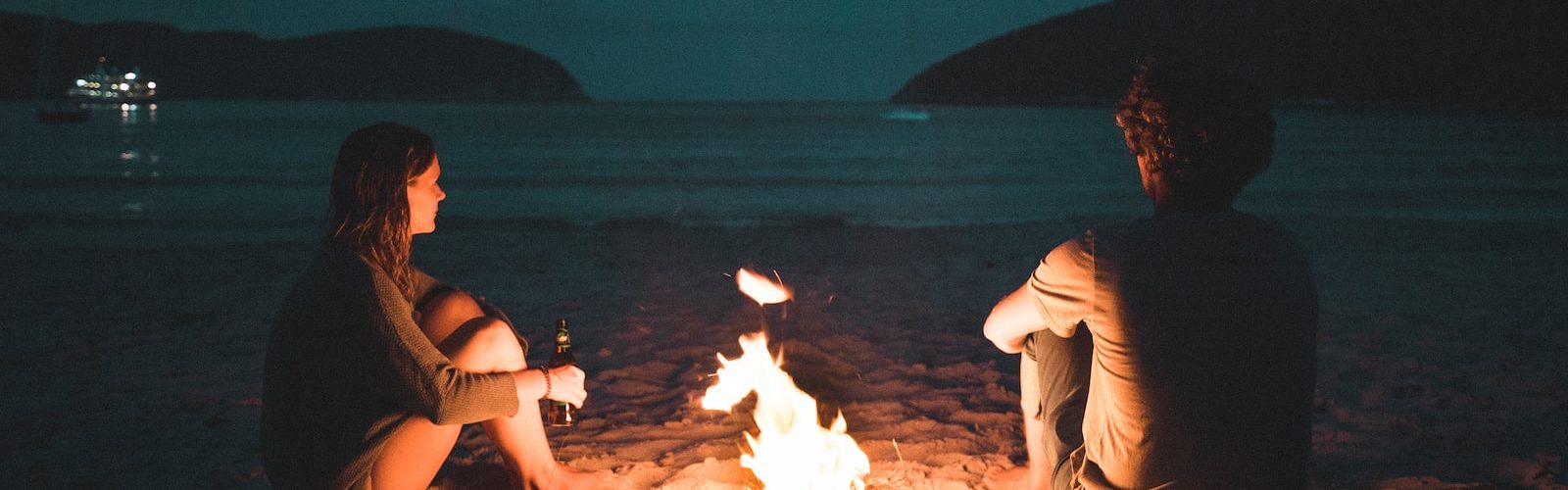 man and woman with bone fire sitting on seashore