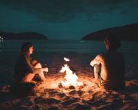 man and woman with bone fire sitting on seashore