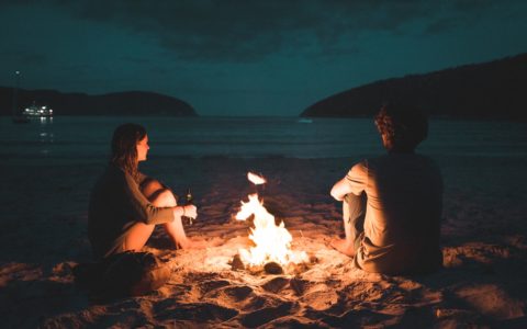 man and woman with bone fire sitting on seashore