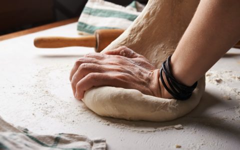 person making dough beside brown wooden rolling pin