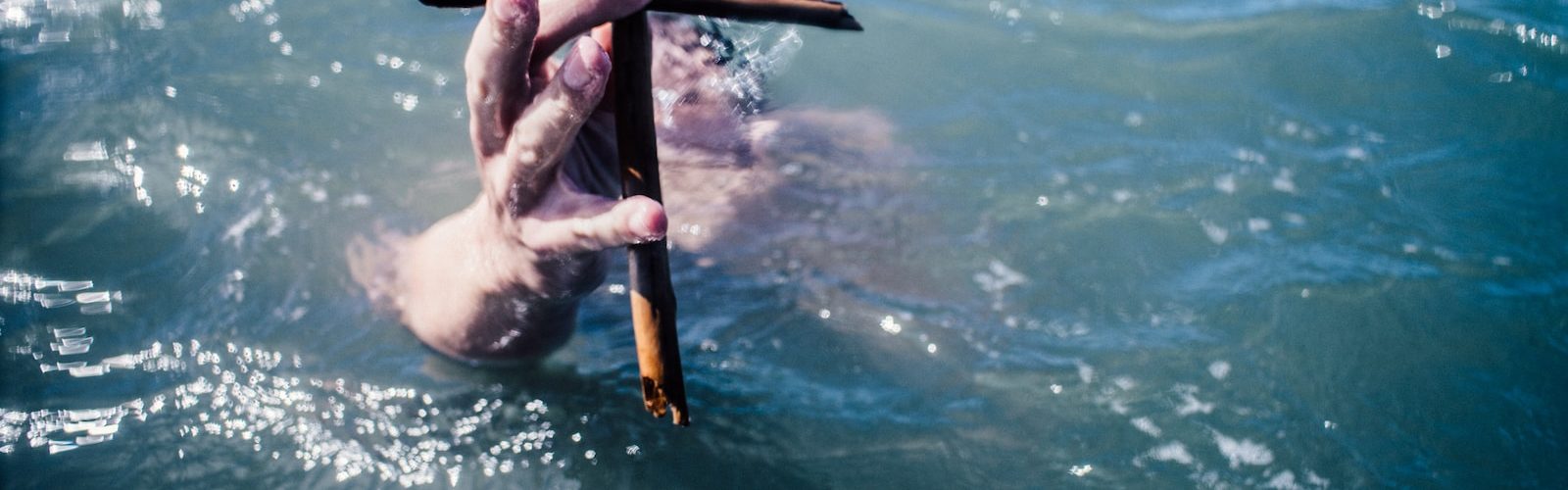 person under water holding brown wooden cross above water at daytime