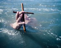 person under water holding brown wooden cross above water at daytime