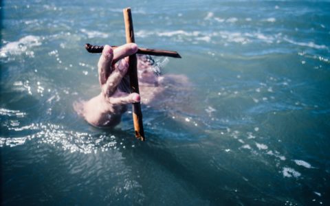 person under water holding brown wooden cross above water at daytime