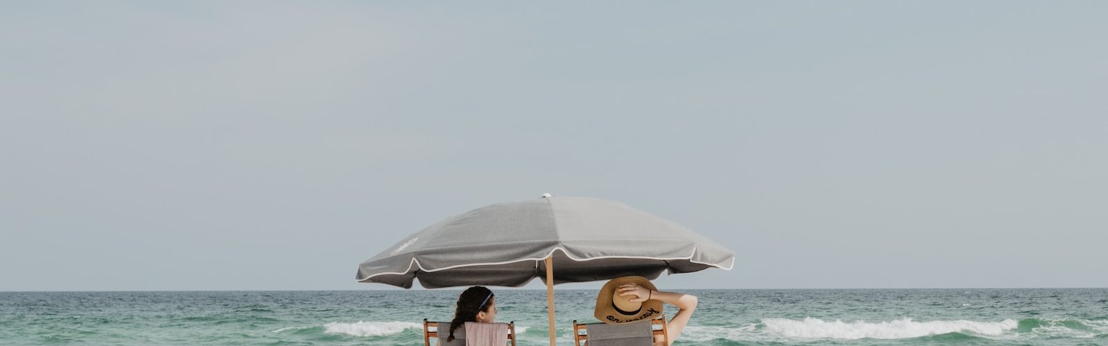 two people under beach umbrella near shoreline