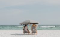 two people under beach umbrella near shoreline