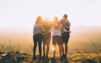 four person hands wrap around shoulders while looking at sunset