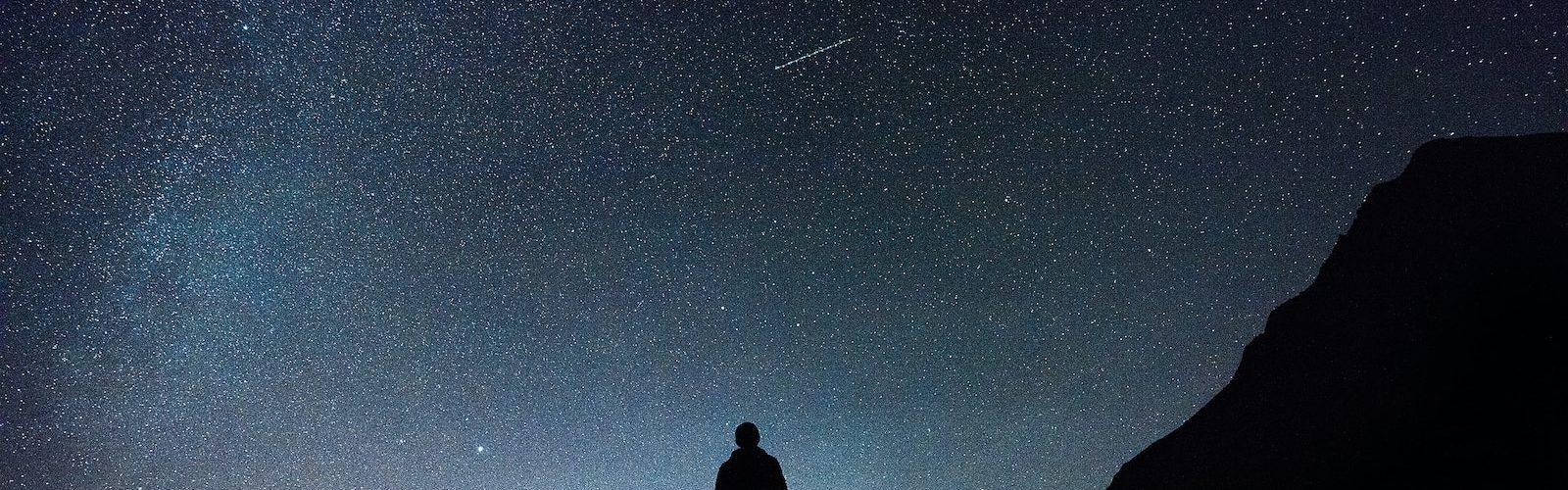 silhouette of man standing on hill during starry night