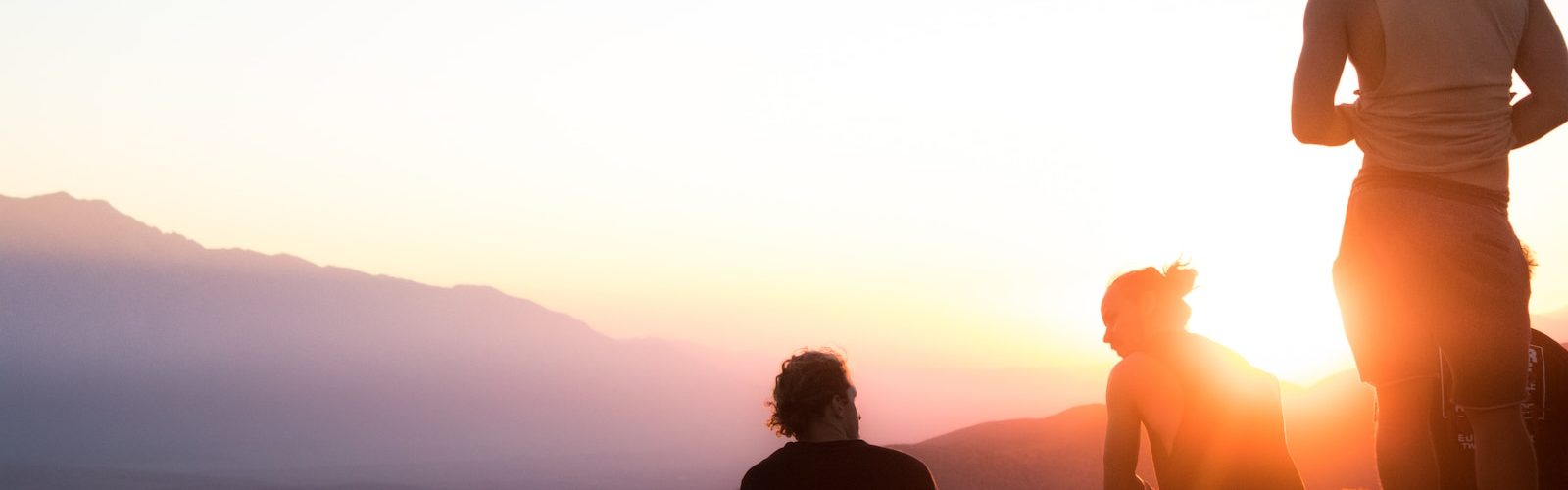 two men sitting and one man standing near cliff taken during golden hour