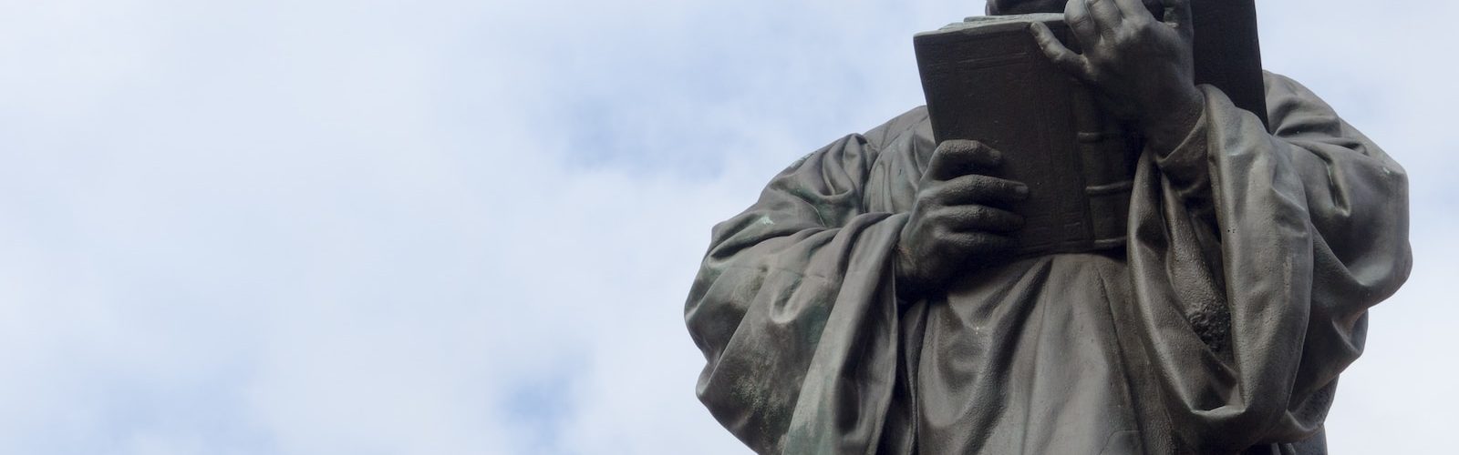 man holding book statue under white clouds during daytime