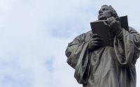 man holding book statue under white clouds during daytime